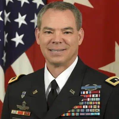 Bert Mizusawa, formal portrait in Army dress uniform with service ribbons, the U.S. flag and a red flag behind him.