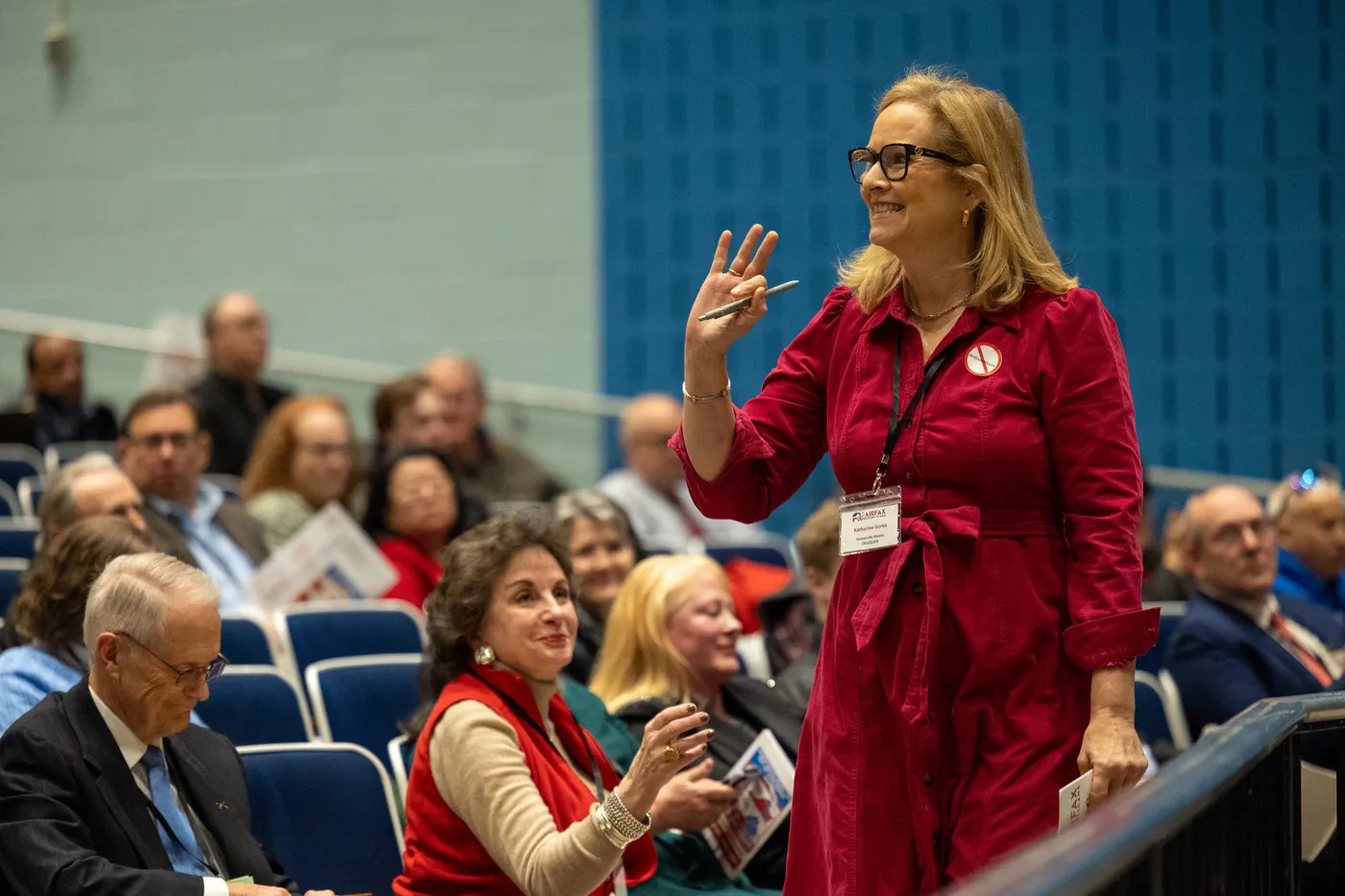 A committee member in red waves to the crowd at the 2026 Fairfax County Republican Convention.